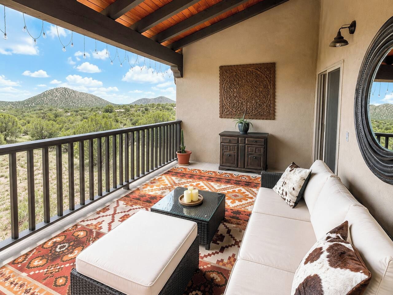 A balcony with a view of a mountainous landscape, a sofa set, a small table with candles, and a decorative wall piece.