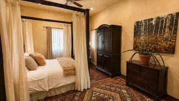 Quarto com cama de dossel, cômoda de madeira escura, pintura grande e tapete estampado.