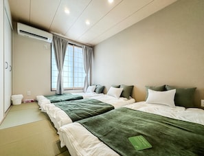 Ein Hotelzimmer mit zwei Betten, einem fensterbelaubten Fenster, einer Klimaanlage und einem Tatami-Boden.