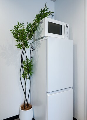 Ein weißer Kühlschrank mit integriertem Mikrowellenofen darüber, neben einem Blumentopf mit grünen Blättern.