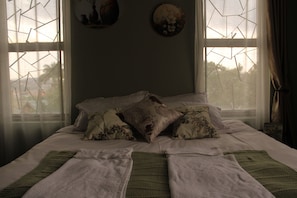 A bed with multiple pillows and a blanket, a wall with a decorative plate, and a window with a geometric pattern. - A Comfy 1-bedroom apartment in central Kampala perfect for your stay! (Kampala)
