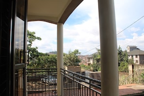 A balcony with a view of a residential area, a metal railing, and a tiled floor. - A Comfy 1-bedroom apartment in central Kampala perfect for your stay! (Kampala)