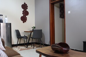 Un espacio habitable compacto con kitchenette, un comedor con dos sillas, una mesa de madera y un adorno en la pared.