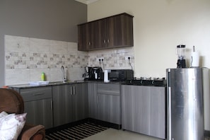 A compact kitchen with dark wood cabinets, a built-in microwave, a coffee maker, and a refrigerator. - A Comfy 1-bedroom apartment in central Kampala perfect for your stay! (Kampala)