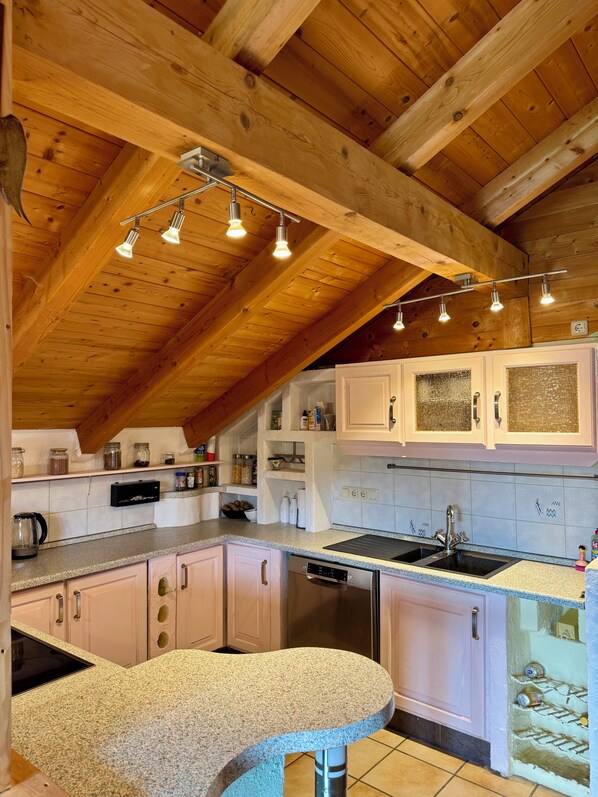 Una cucina con travi in legno, un piano di lavoro in granito, mobili bianchi e una lavastoviglie.