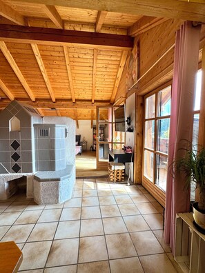 A spacious room with a wooden ceiling, a stone fireplace, and a large window with curtains. - Starting Feb. 27: Vacation rental on the edge of the forest; dogs welcome upon request; not centrally located (Halsbach)