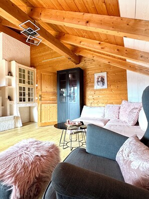 Un accogliente interno di una baita con soffitto in legno, un divano, un mobiletto e un tappeto soffice.