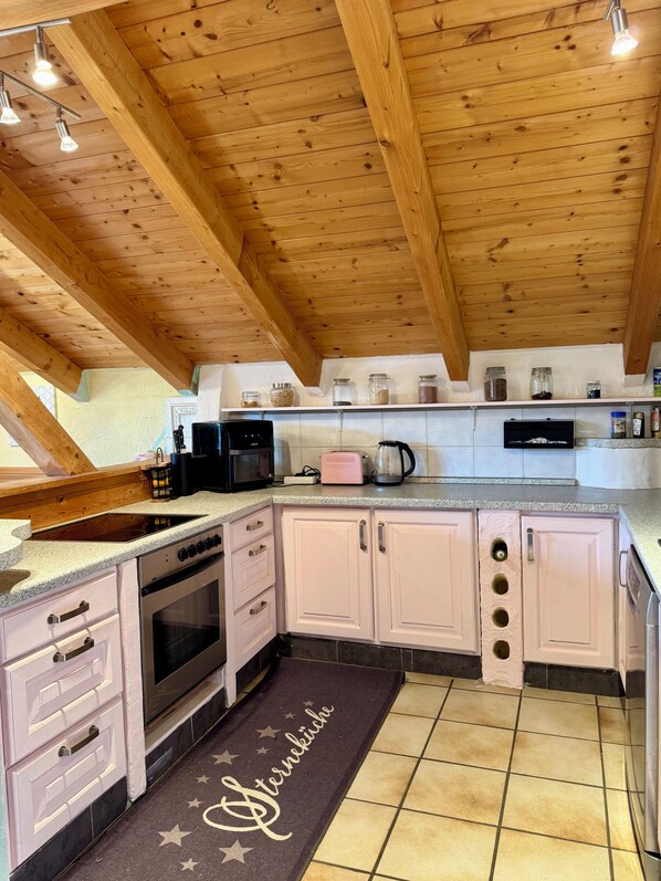 A kitchen with wooden beams, a stove, cabinets, and a countertop with various appliances. - Starting Feb. 27: Vacation rental on the edge of the forest; dogs welcome upon request; not centrally located (Halsbach)