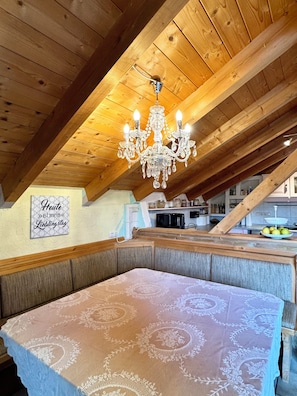Una camera mansardata accogliente con soffitto in legno, un lampadario, una panca e un tavolo con tovaglia fantasia.