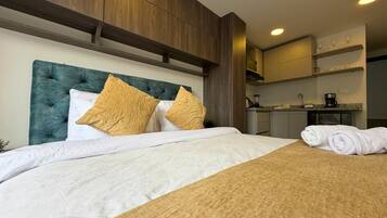Een hotelkamer met een bed, hoofdeinde, een kitchenette en een set handdoeken.