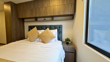 Une chambre d’hôtel avec un grand lit, une tête de lit en bois et une petite table de chevet agrémentée d’une plante.