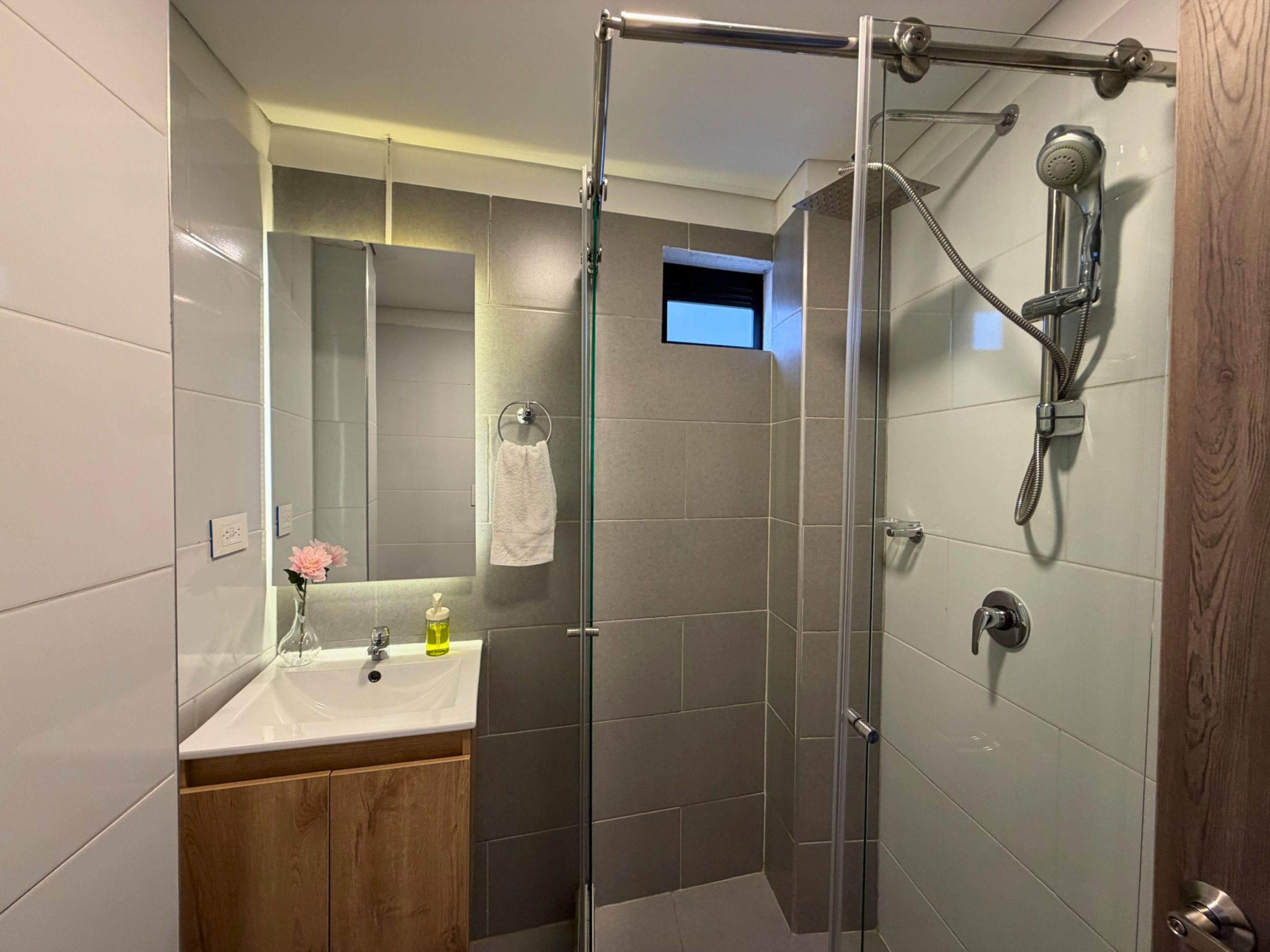 Un baño moderno con ducha envuelta en vidrio, un lavamanos con espejo y un mueble de tocador de madera.