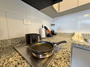 A kitchen with a granite countertop, a stove, a frying pan, a pot, a blender, and a knife block. - Nook Galerías by Renteo (Bogotá)