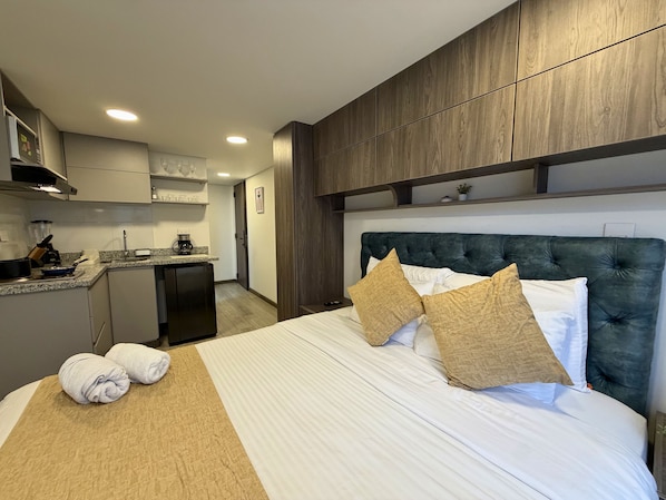 A hotel room with a bed, a kitchenette, and a view of the hallway. - Nook Galerías by Renteo (Bogotá)