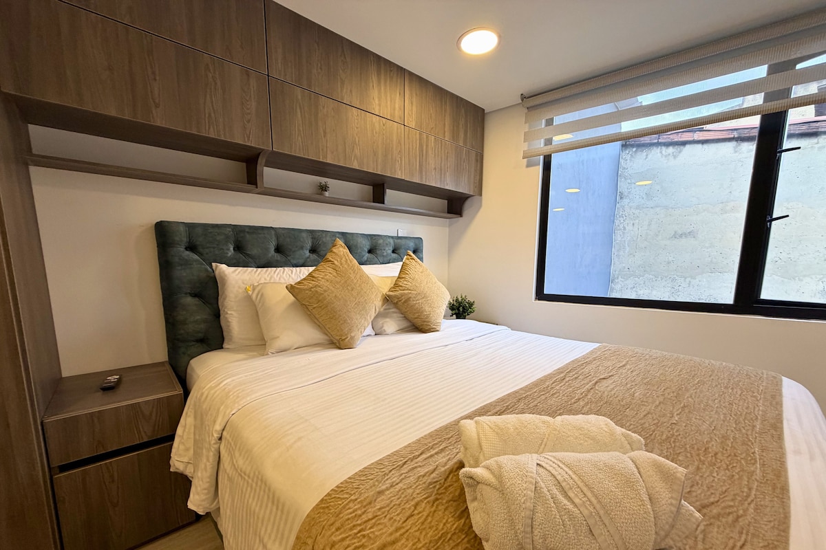 A modern bedroom with a tufted headboard, a large window, and a neatly made bed with a beige and brown color scheme.