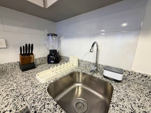 A kitchen with a granite countertop, a stainless steel sink, a black blender, a knife block, and a coffee maker. - Nook Galerías by Renteo (Bogotá)