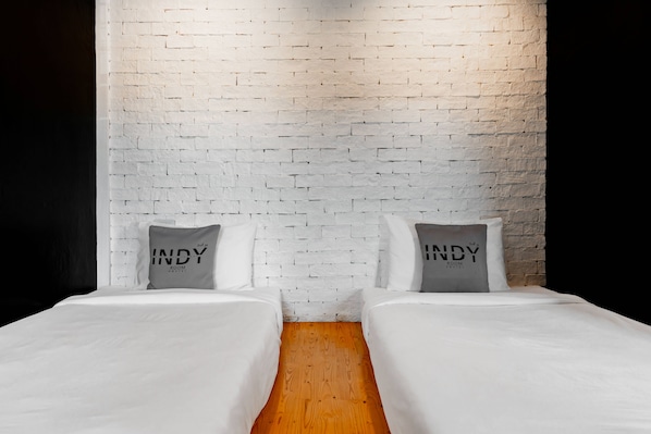 A hotel room with two beds, white bedding, and pillows with 'INDY ROOM HOSTEL' text.