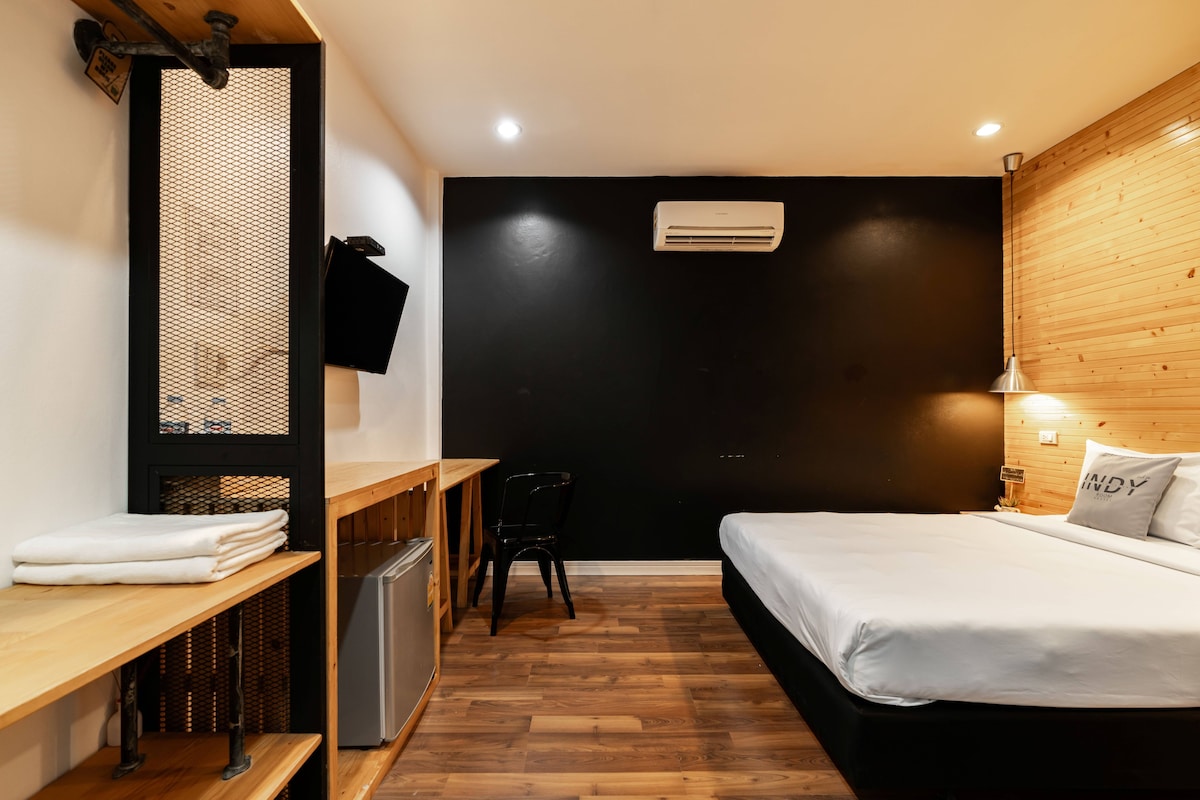 Une chambre d’hôtel de taille réduite, comprenant un lit, un bureau, une chaise et une petite kitchenette.