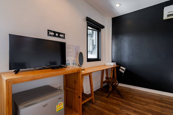 A room with a wooden desk, a television, a window with blinds, a black wall, and a small heater.