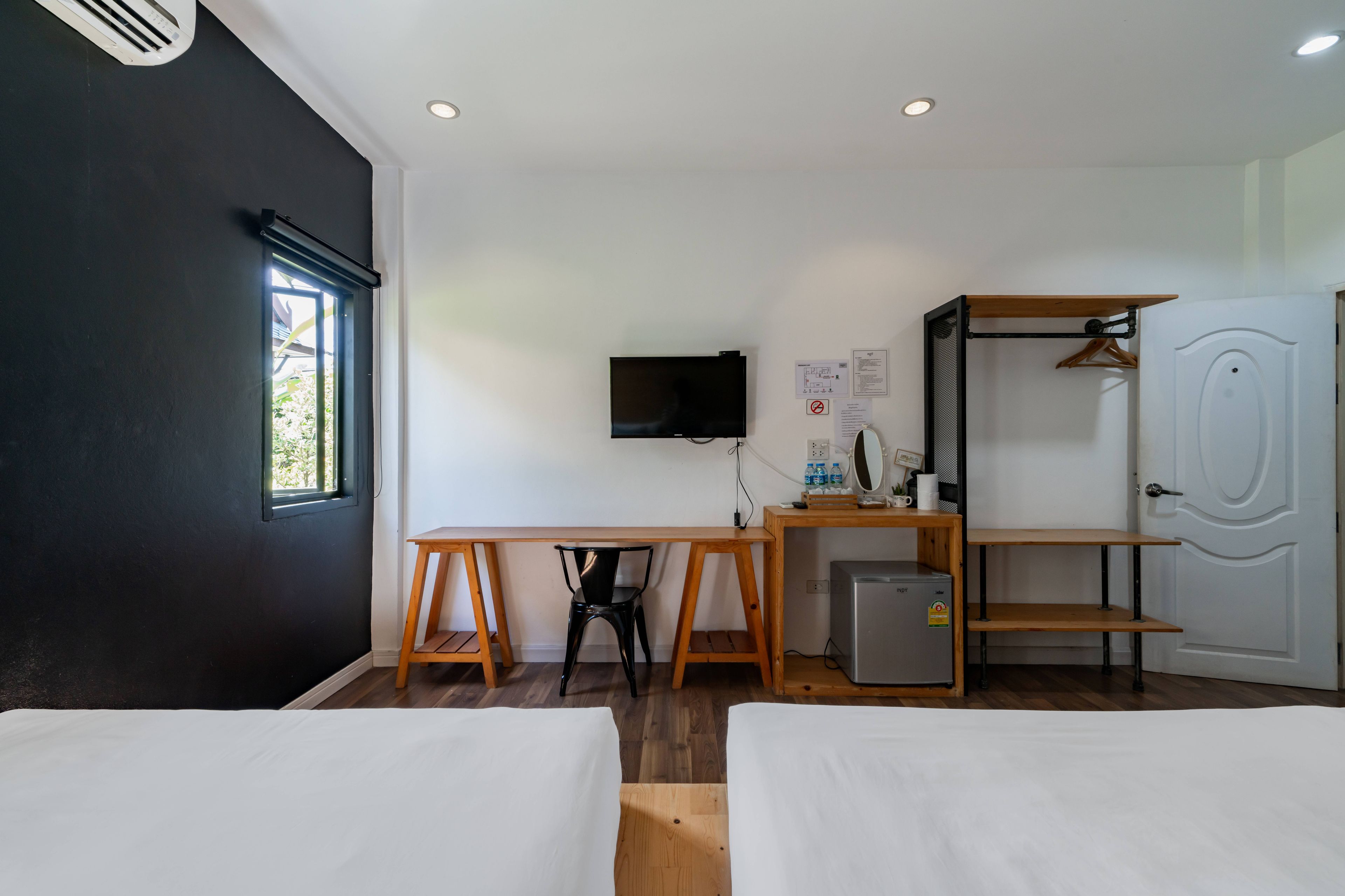 Una habitación con dos camas, un escritorio, televisor, un refrigerador pequeño y un armario.