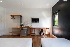 A room with a desk, two beds, a TV, and a window.
