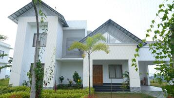 A modern two-story house with a white exterior, a sloped roof, and a small garden with various plants and flowers.