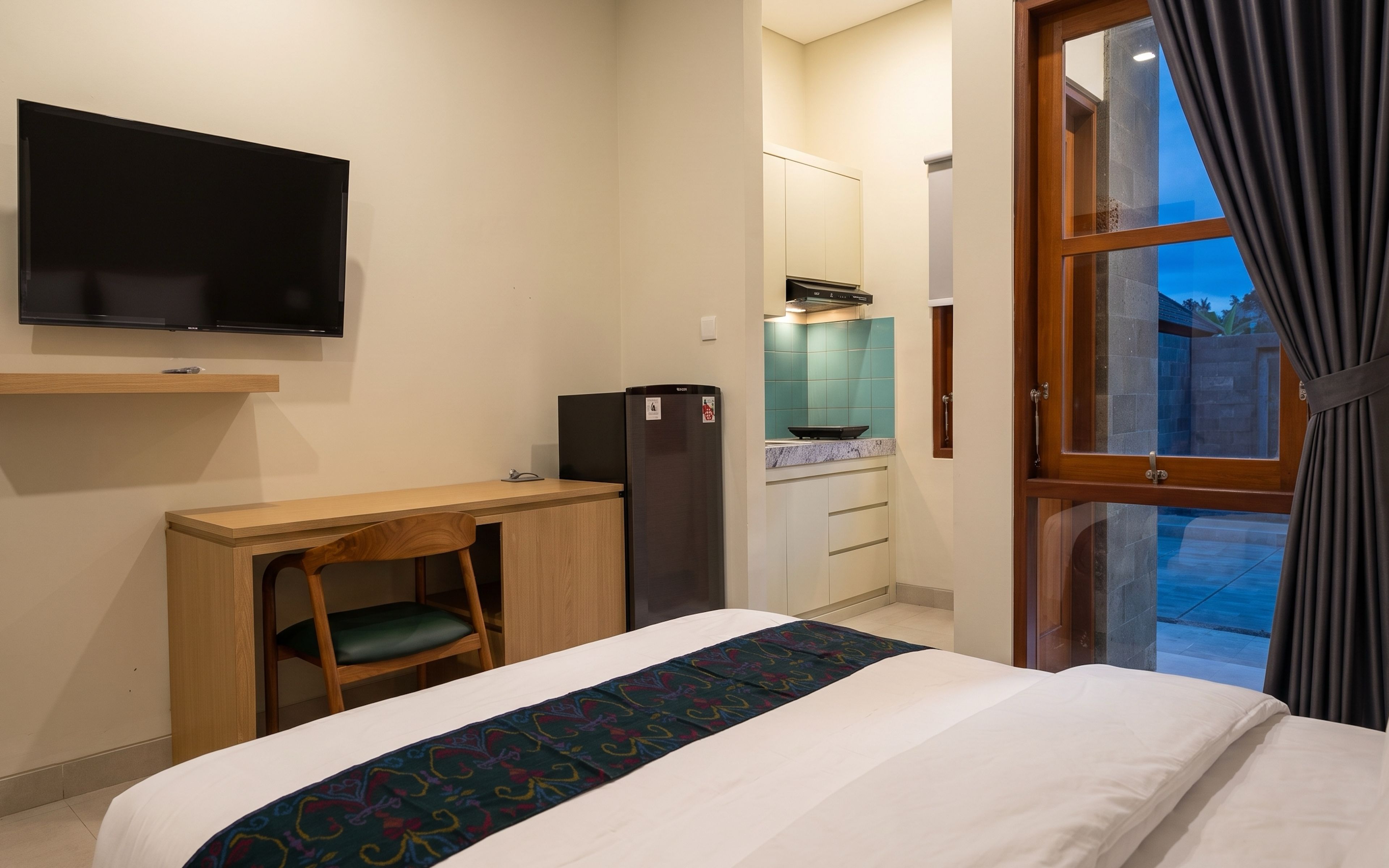 A hotel room with a bed, a desk, a television, a refrigerator, and a window with curtains.