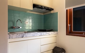 Una cocina con baldosas color turquesa, un lavamanos de acero inoxidable, una campana extractora negra y una ventana con marco de madera.