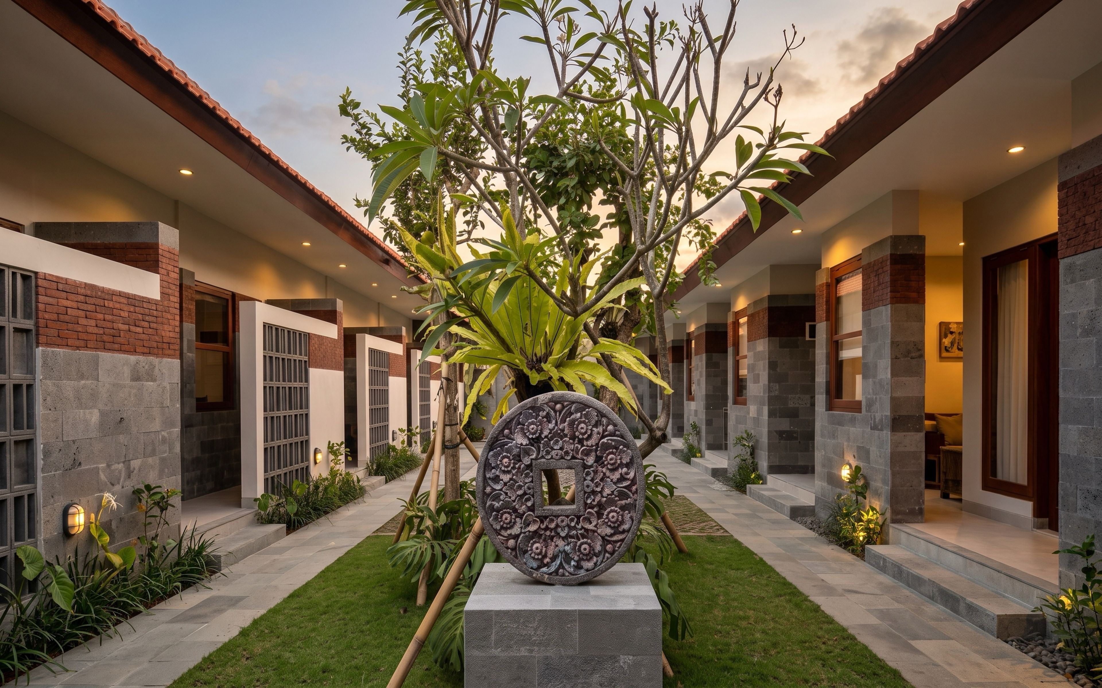 A modern building with a central garden, featuring a decorative stone centerpiece, and a pathway leading to the entrance.