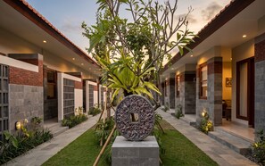 Un edificio moderno con un jardín central, que cuenta con una pieza central decorativa de piedra y un camino que lleva a la entrada.