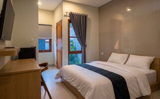 Quarto de hotel com cama, escrivaninha, cadeira, televisão e janela com cortinas.