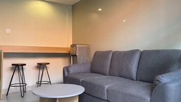 A modern living area with a grey sofa, two wooden stools, a round coffee table, and a built-in espresso machine.
