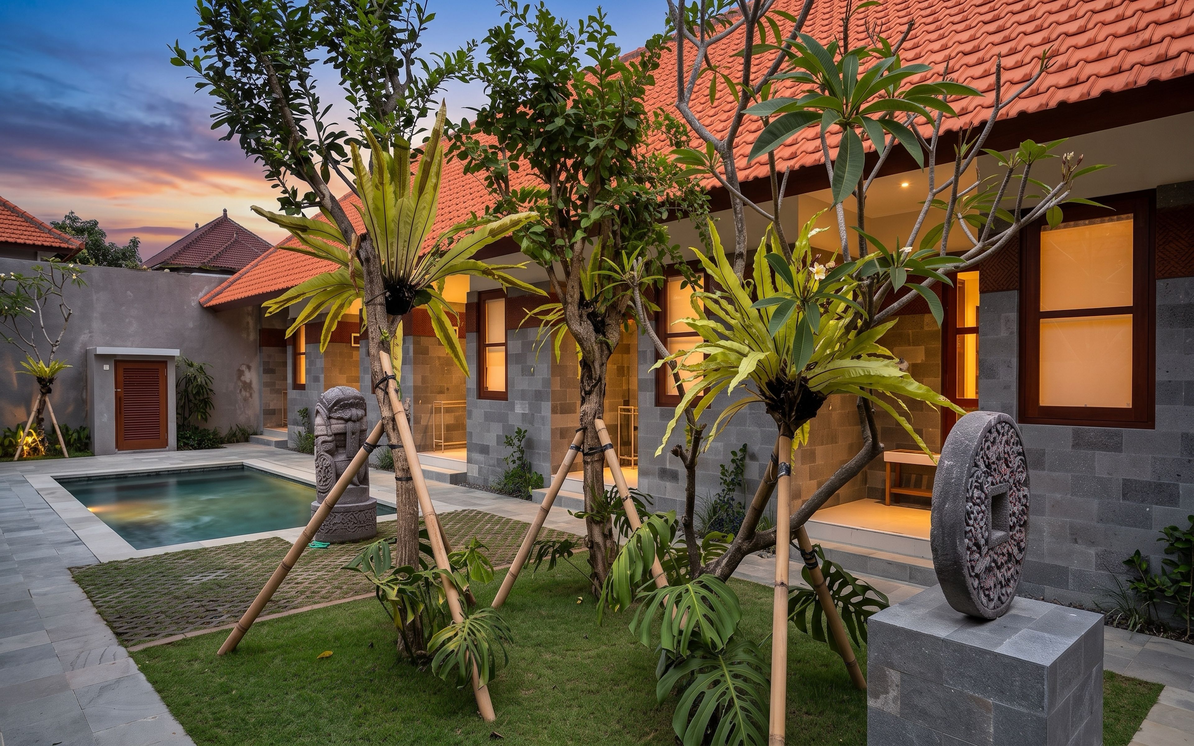 A modern house with a swimming pool, surrounded by tropical plants and a stone pathway.