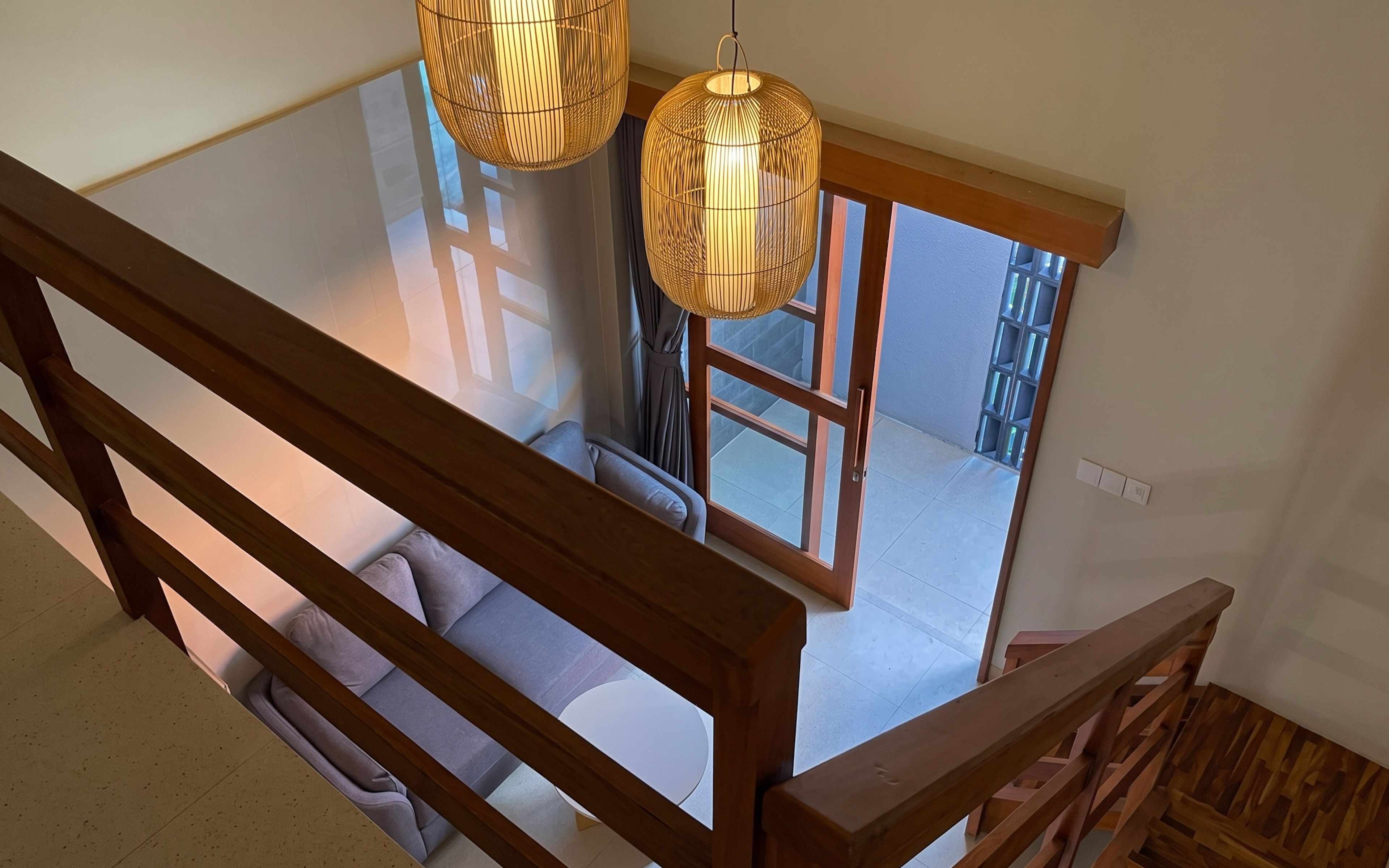 A wooden staircase leading to a room with a sofa and two hanging lamps.