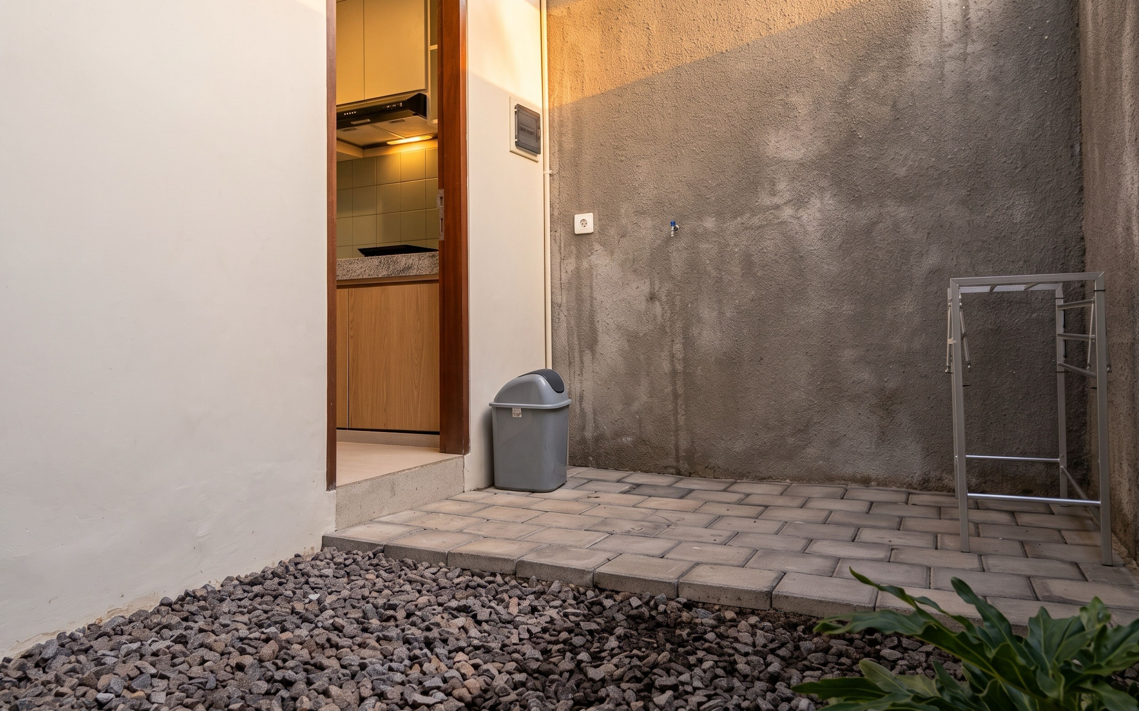 A small outdoor area with a concrete wall, a metal ladder, a trash bin, and a paved floor.
