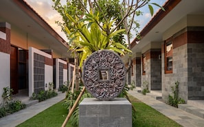 Un edificio moderno con un patio central, que presenta una escultura decorativa de piedra, un césped cuidado y un sendero que conduce a la entrada.
