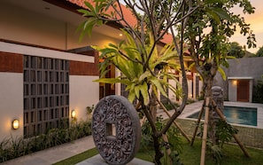 Un espacio exterior moderno con piscina, escultura de piedra y plantas tropicales.