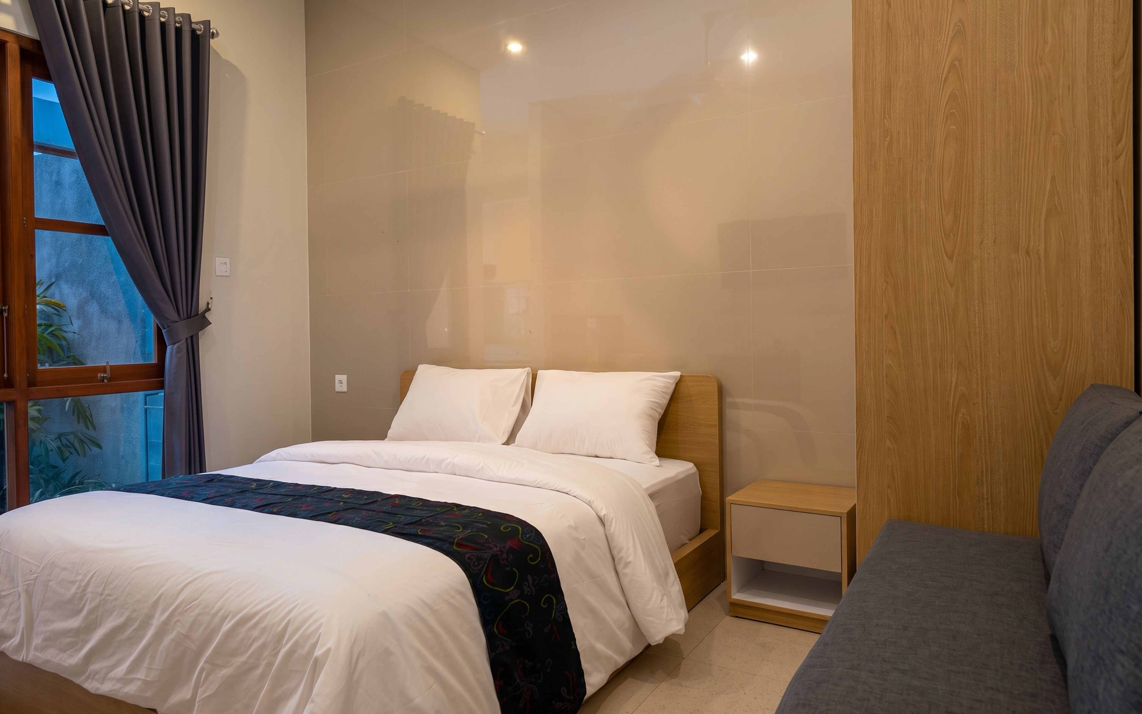 A bedroom with a bed, bedside table, and a grey sofa.