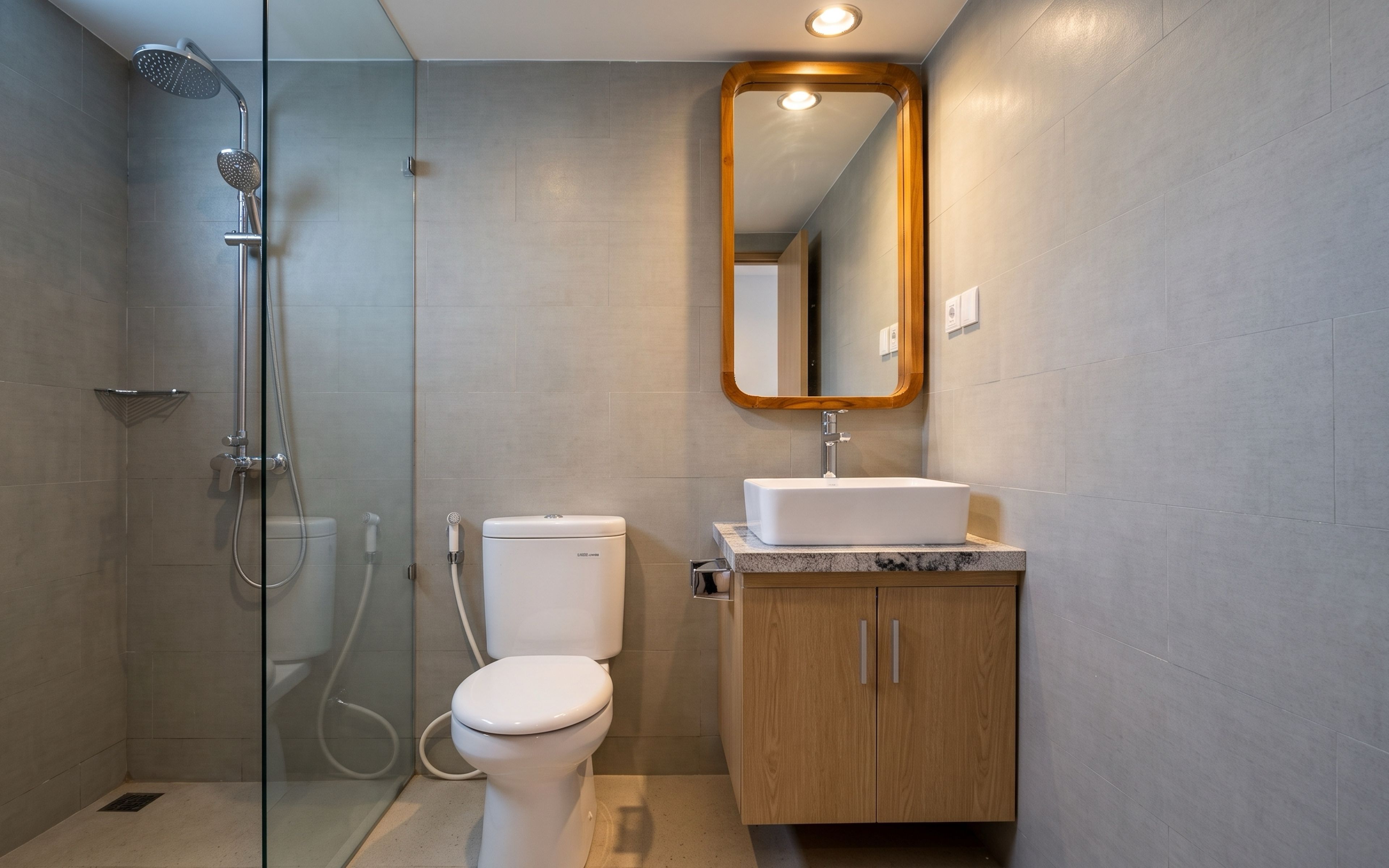 A modern bathroom with a glass-enclosed shower, a toilet, a sink with a wooden cabinet, and a mirror with a wooden frame.