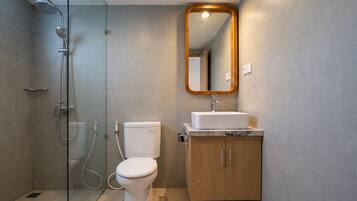 A modern bathroom with a glass-enclosed shower, a toilet, a sink with a wooden cabinet, and a mirror with a wooden frame.