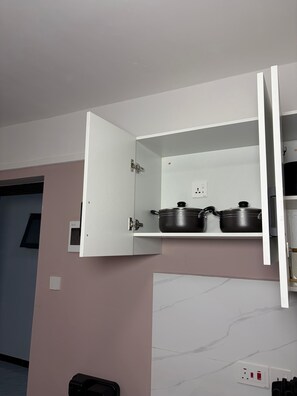 A kitchen with a white cabinet containing pots and pans, a marble backsplash, and a wall-mounted electrical outlet. - TALANTA SKYLINE ONE BEDROOM ALONG NGONG ROAD, NEAR JUNCTION MALL (Nairobi)