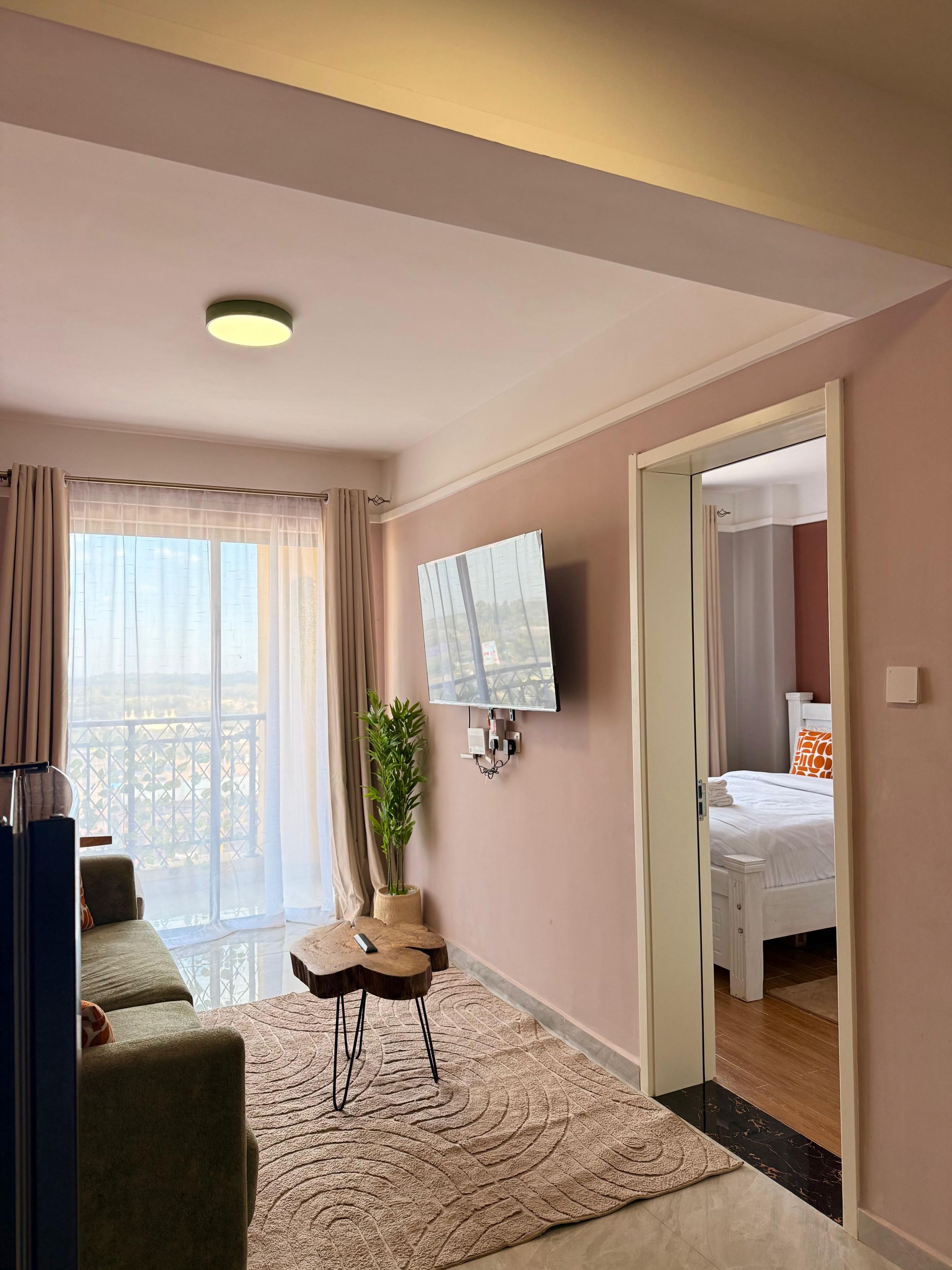 Een hotelkamer met een bed, een aan de muur bevestigde televisie, een tafeltje met een plant en uitzicht op het landschap door het raam.