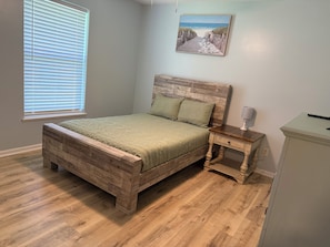 Une chambre à coucher avec un lit en bois, une table de chevet, une lampe et un tableau représentant une scène de plage.