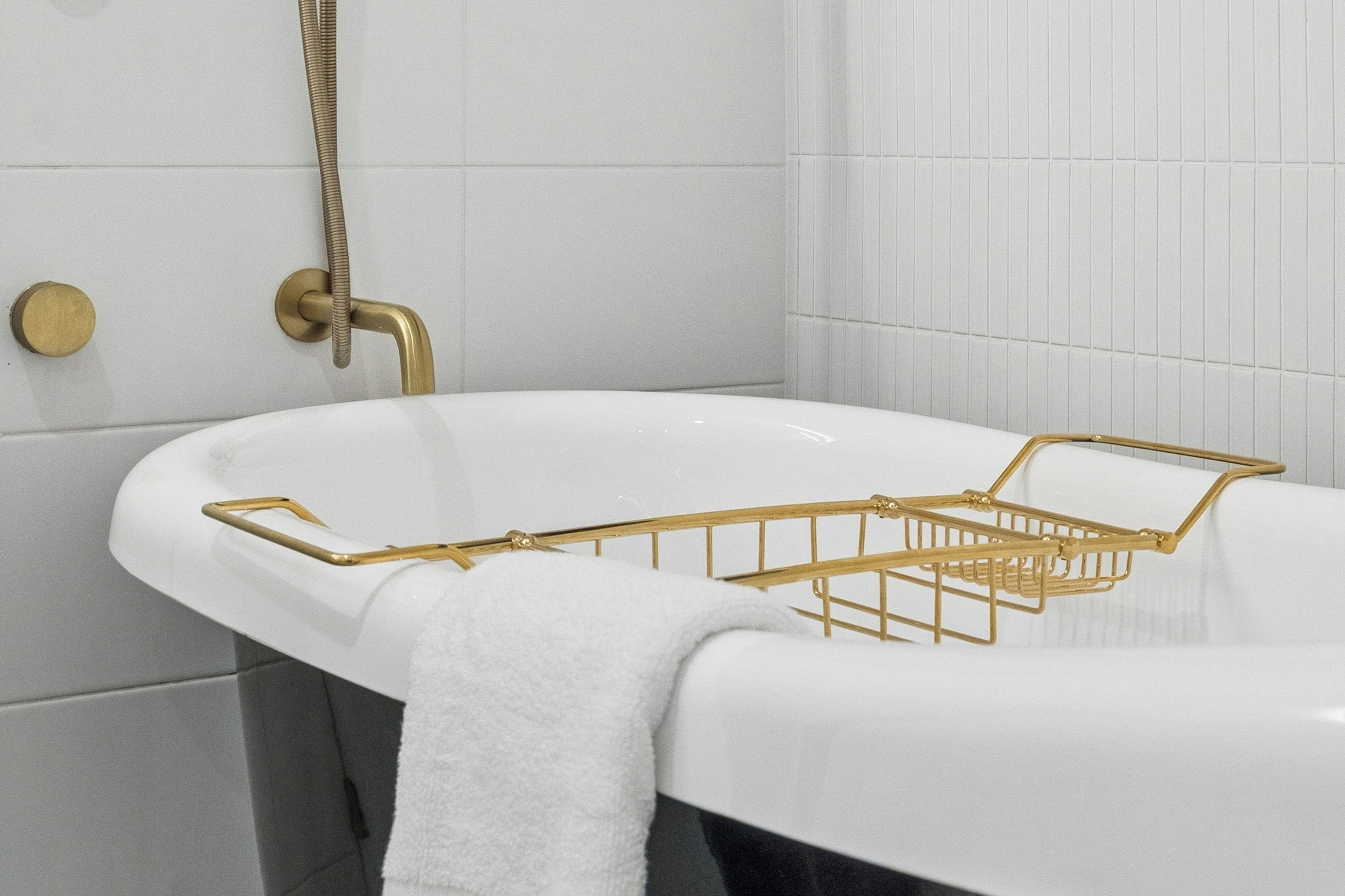 A bathroom with a white bathtub, a gold showerhead, and a gold towel rack.