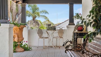 A covered patio with two metal chairs, a table, a potted plant, and a bench.