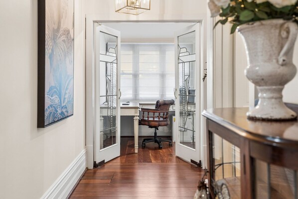 A hallway with a wooden floor leading to a room with a desk and chair.