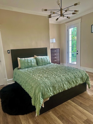 A bedroom with a bed, a dresser, a lamp, and a door leading to a balcony. - Cozy Retreat (St. Louis)