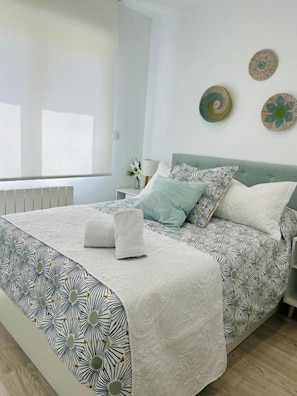 A neatly made bed with a patterned bedspread, a bedside table with a lamp, and decorative wall plates. - DELUXE FAMILIAR  (Albacete)