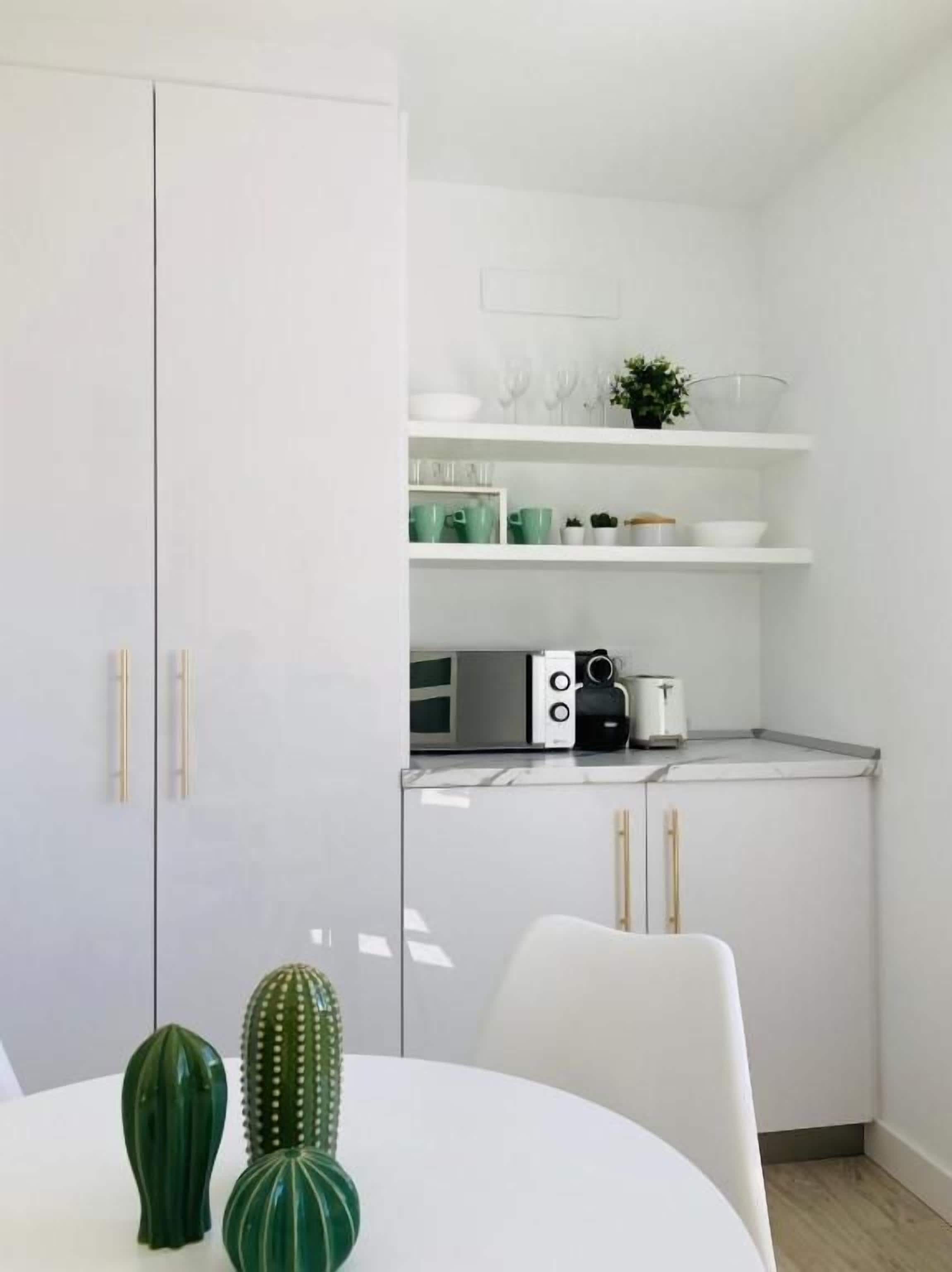 Una cocina moderna con armarios blancos, una mesa de comedor blanca y una decoración de cactus.