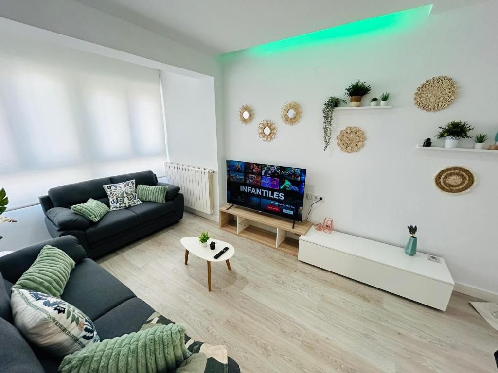 Ein modernes Wohnzimmer mit einem Flachbildfernseher, schwarzen Sofas, einem Couchtisch und dekorativer Wandkunst.